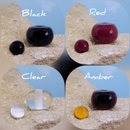 Collage of ashes in glass beads and charms on a textured surface with colour labels, black, red, clear and amber.