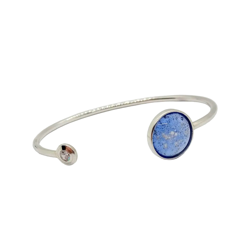 A solid silver ashes solitaire bangle featuring a blue glass bead centerpiece with a small cubic zirconia on the side on a white background 