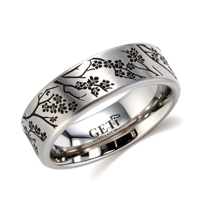 Satin titanium flat-profile silver-coloured ashes ring featuring intricately engraved cherry blossoms and branches of a tree circulating the ring.  Photographed on a white background.