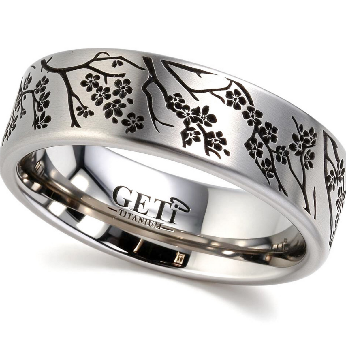 Satin titanium flat-profile silver-coloured ashes ring featuring intricately engraved cherry blossoms and branches of a tree circulating the ring.  Photographed on a white background on a tilted right angle.