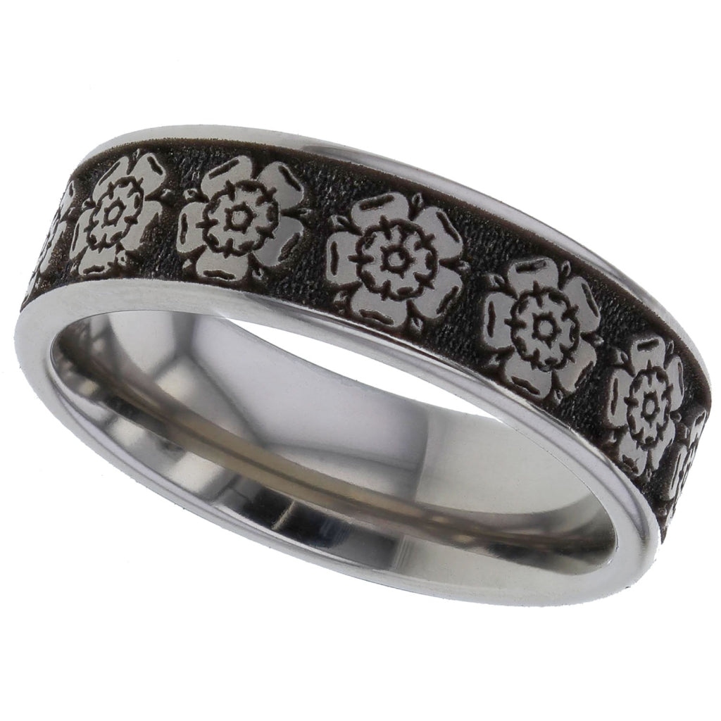 A silver-toned titanium metal band ring for cremation ashes featuring a textured black inlay with embossed floral rose motifs, shown on a plain white background.