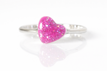 Silver ring with pink glittery heart-shaped stone on a white background