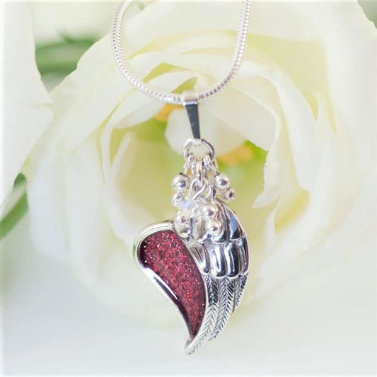 Silver Angel Wing placed over a heart shaped red inlay with snake chain on a cream rose background.