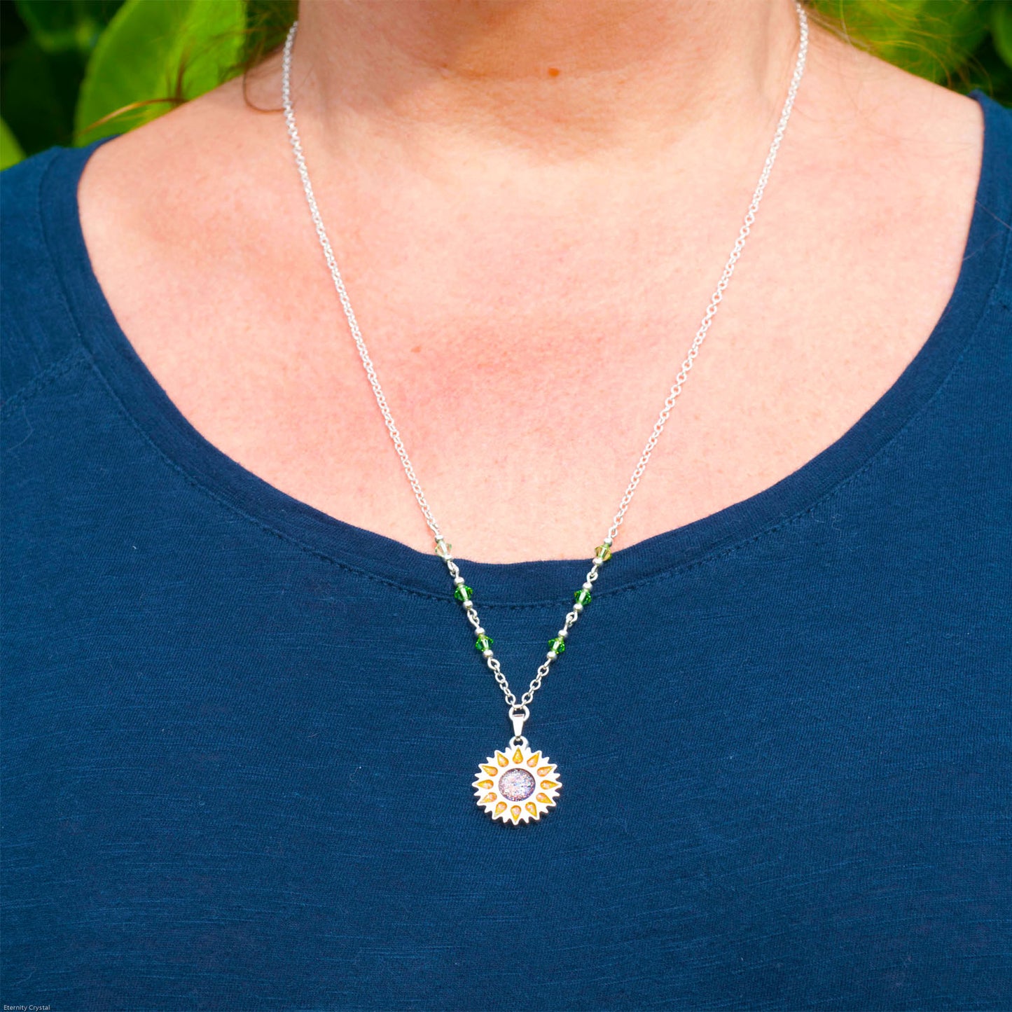 Sunflower pendant with sparkling yellow petals and a round sparkling warm orange centre on a silver long chain with green beads being worn round a ladies chest wearing navy plain top 