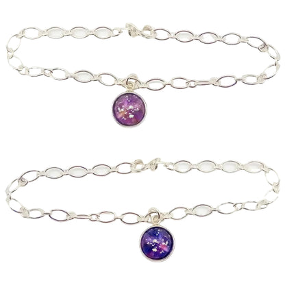 Two silver chain memorial bracelets with a circular glass charm bead with ashes held  in pink glass and purple glass within a silver cabochon, on a white background.

