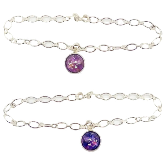 Two silver chain memorial bracelets with a circular glass charm bead with ashes held  in pink glass and purple glass within a silver cabochon, on a white background.

