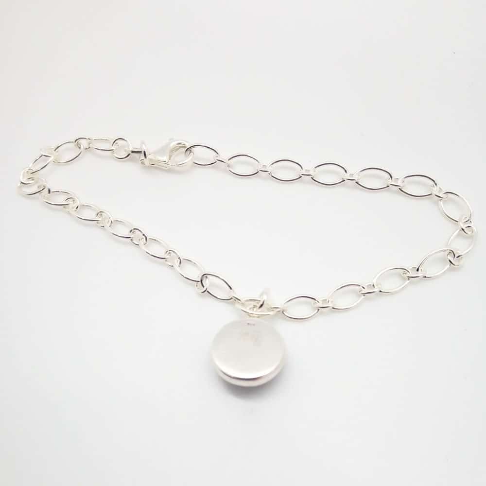 Reverse side of silver chain memorial bracelet with a circular bead for ashes held in a silver cabochon on a white background.