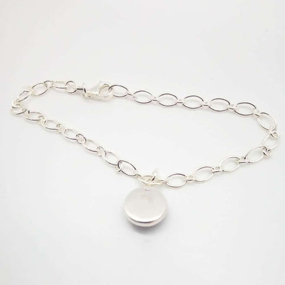 Reverse side of silver chain memorial bracelet with a circular bead for ashes held in a silver cabochon on a white background.