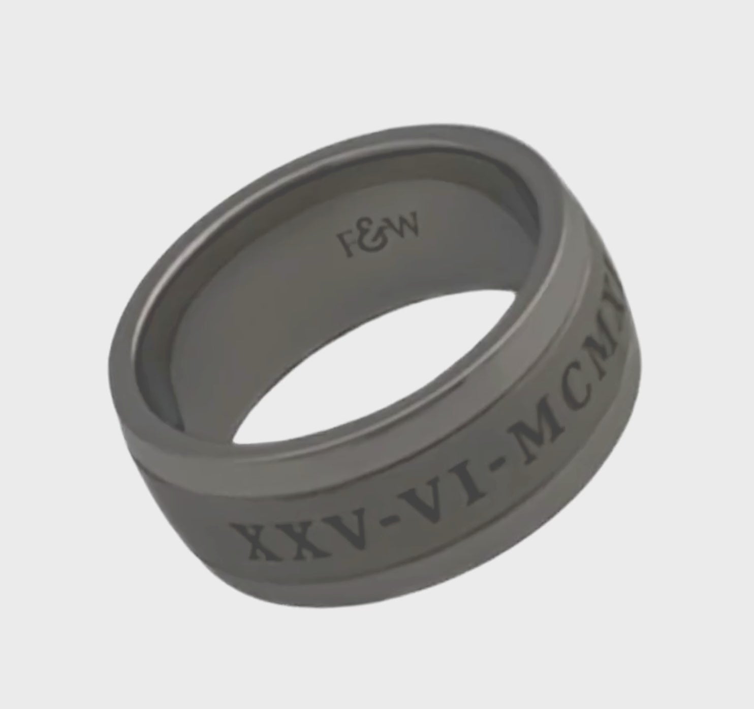 Video of titanium ashes ring with engraved date in roman numerals on a plain white background showing the ringside profile 